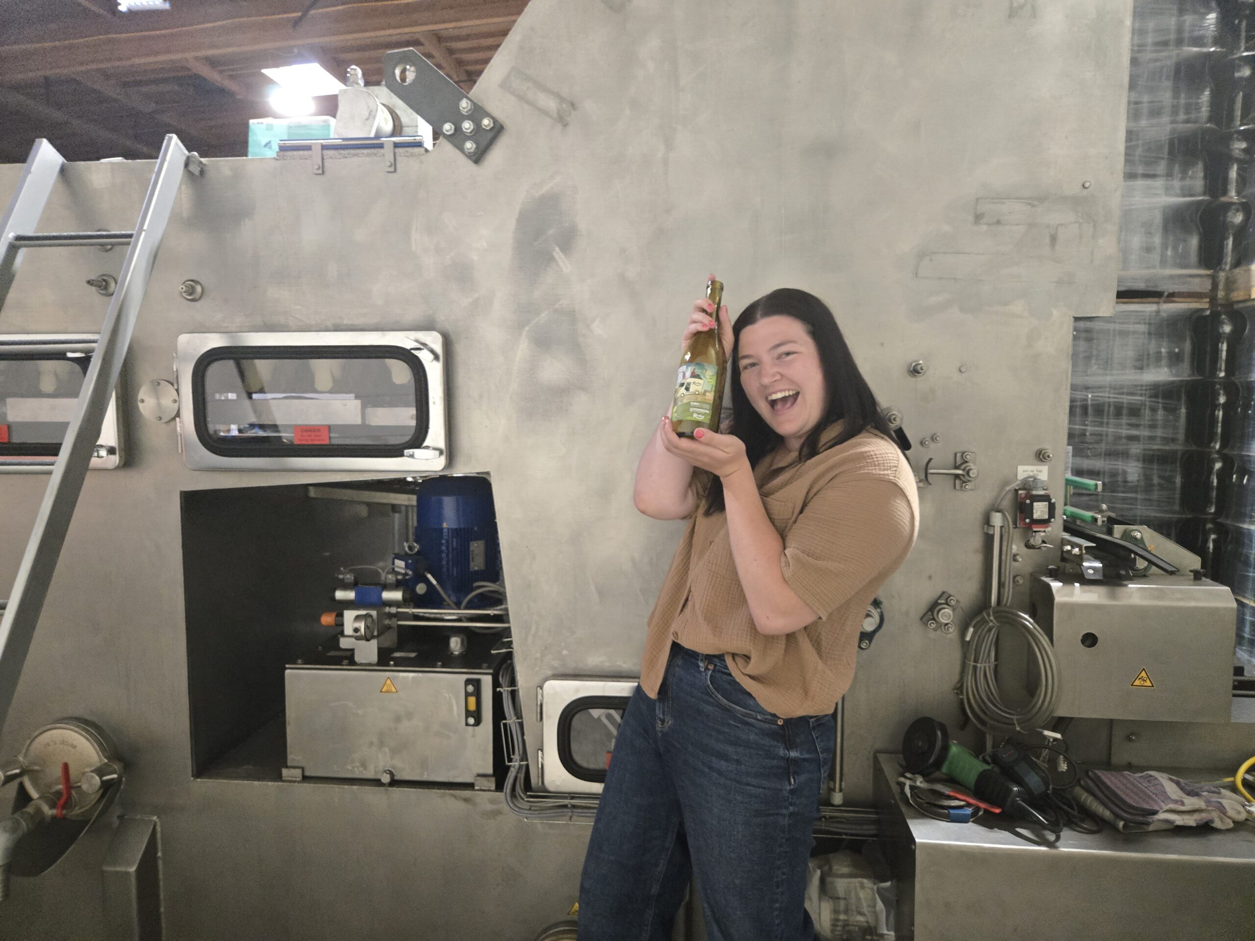 Revino Intern, Abby Williams, holding a revino bottle in front of bottle washing equipment