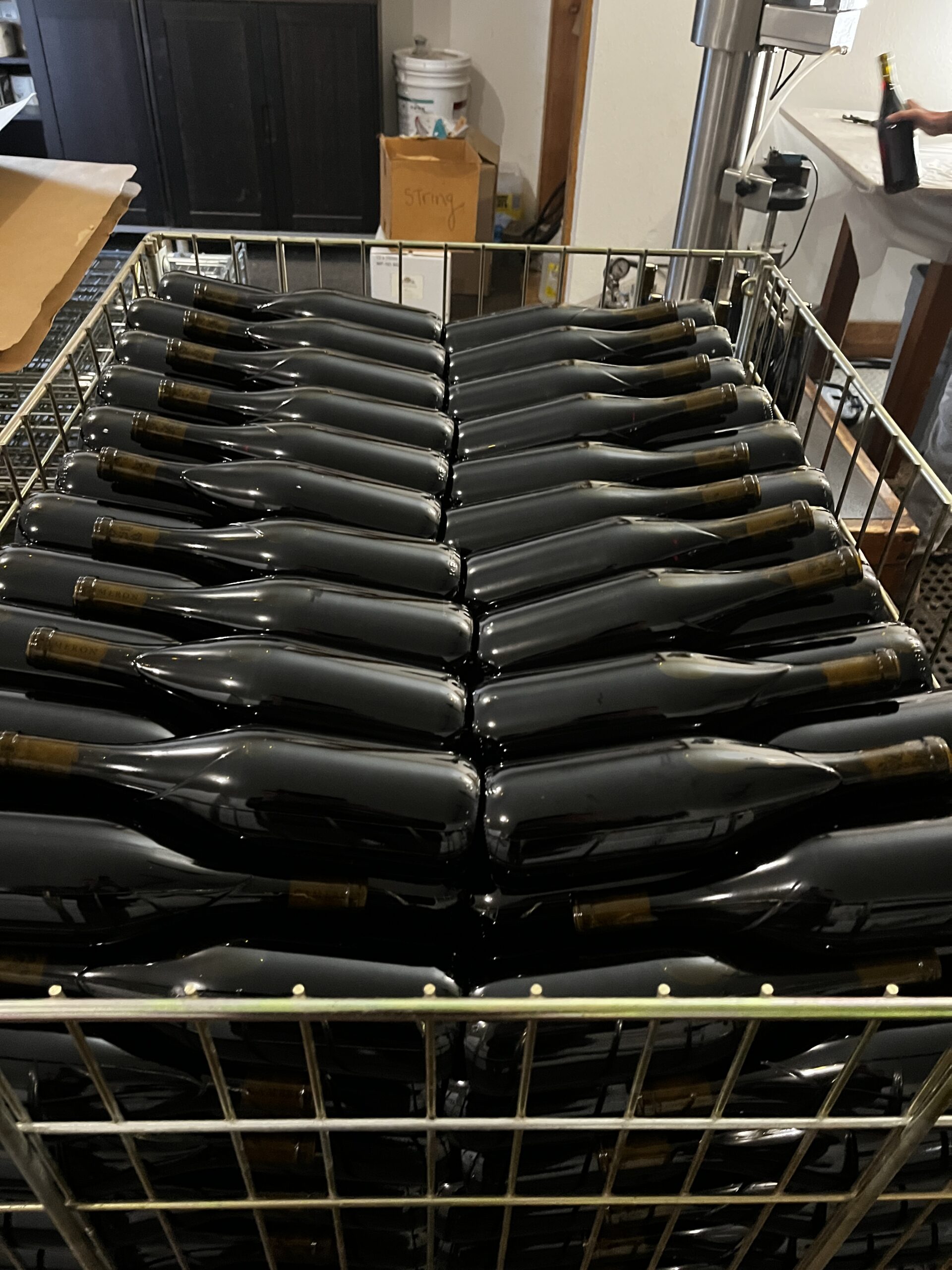 Filled and sealed reusable wine bottles stacked in a wire crate