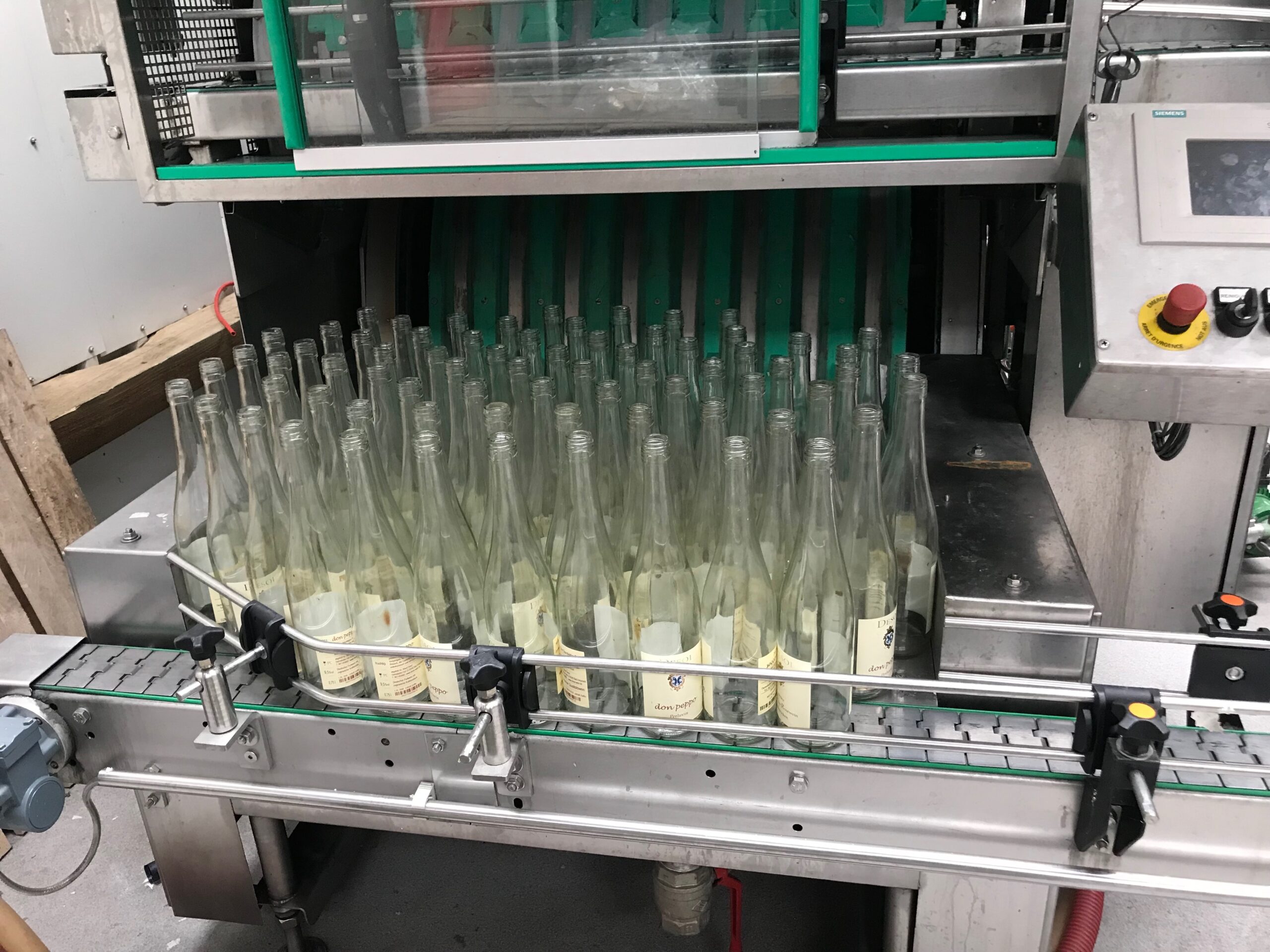 Reusable glass wine bottles lined up on a conveyor entering a bottle washing machine